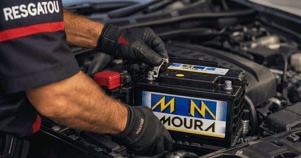 Técnico da Resgatou, de luvas e uniforme, encaixando uma bateria nova no cofre do motor de um carro, com os dois terminais à vista