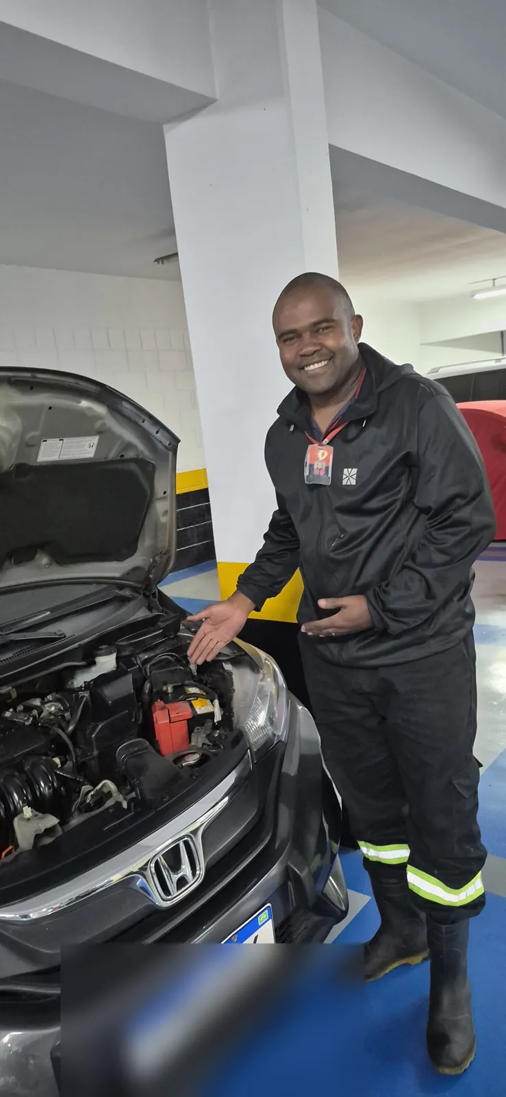 Técnico da Resgatou com crachá de identificação ao lado de um carro com o capô aberto, em garagem de prédio